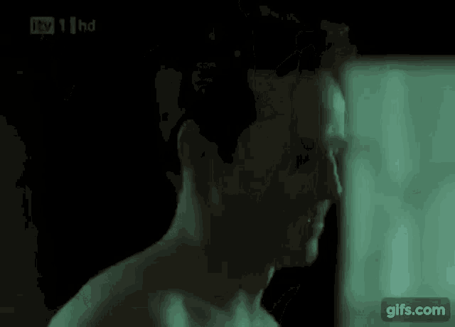 a man without a shirt is standing in a dark room with a green light behind him .