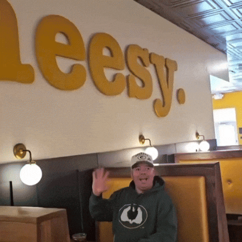 a man in a green bay packers sweatshirt stands in front of a wall that says leesy