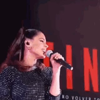 a woman is singing into a microphone in front of a red sign .