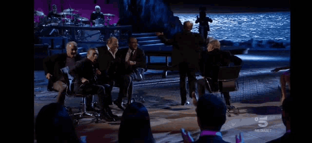 a group of people are sitting in front of a stage with the number 5 on the bottom