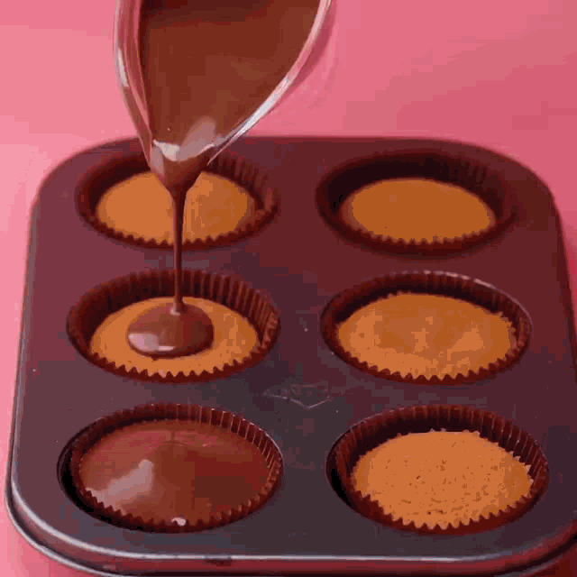 a tray of cupcakes with chocolate being poured into them