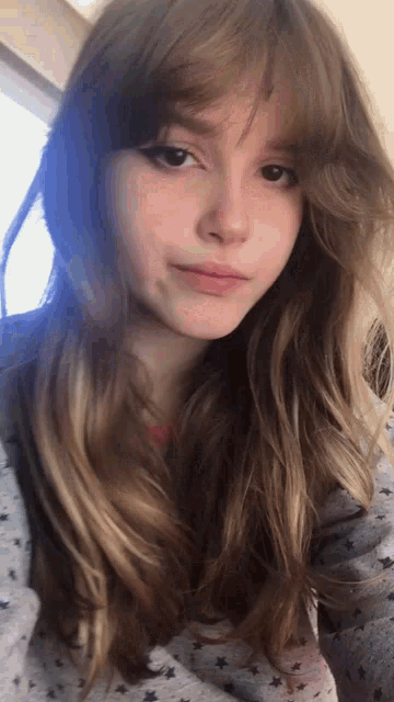 a close up of a woman 's face with long hair and a gray shirt with stars on it .