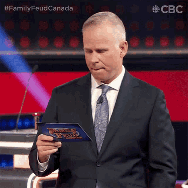 a man in a suit and tie is holding a piece of paper that says family feud canada on it
