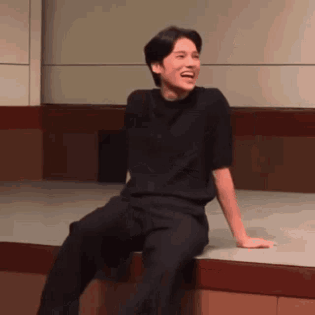 a man in a black shirt and black pants is sitting on a wooden platform .