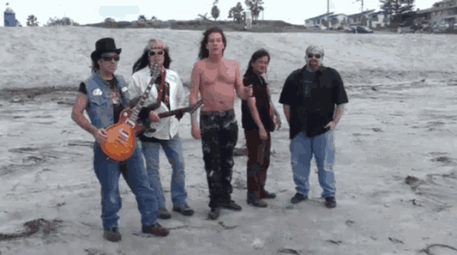 a group of men standing on a sandy beach with one holding a guitar