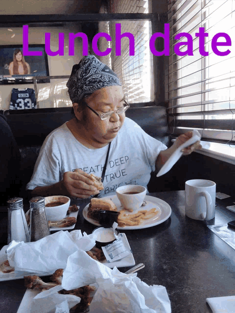 a woman wearing a shirt that says " eat deep true " is sitting at a table eating lunch