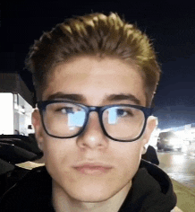 a young man wearing glasses and a black hoodie looks at the camera .