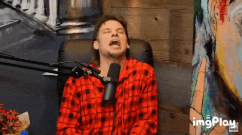 a man in a red and black plaid shirt is sitting in front of a microphone with his mouth open ..