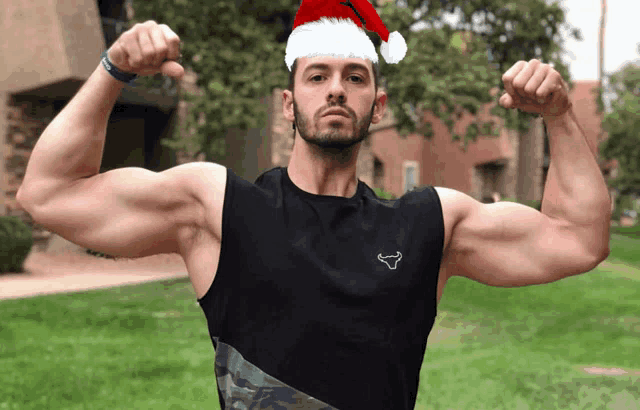 a man wearing a santa hat flexes his muscles in front of a building