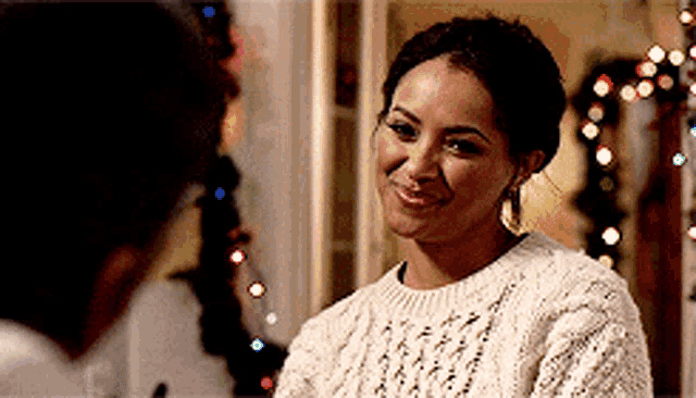 a woman in a white sweater is smiling at a man in front of a christmas tree .