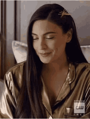 a woman with long hair is smiling and wearing a gold pajama top with a cw logo on it .
