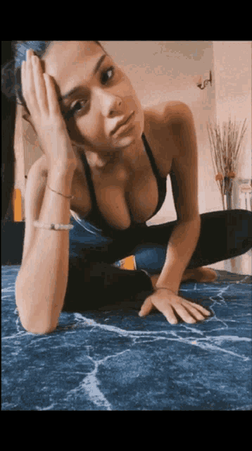 a woman in a sports bra is sitting on the floor with her hand on her face