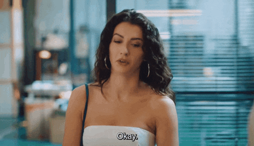 a woman in a strapless top says okay in front of a window