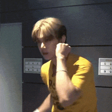 a man in a yellow shirt is standing in front of a wall with a sign that says ' a ' on it