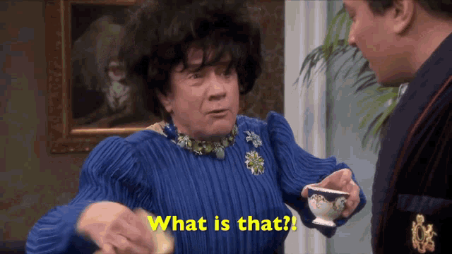a woman in a blue sweater is holding a cup of tea and asking what is that