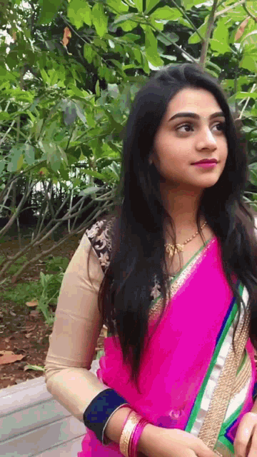 a woman in a pink and green saree stands in front of a bush
