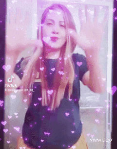a woman in a black shirt is dancing in front of a screen with hearts flying around her .