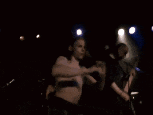a man without a shirt is singing into a microphone while another man plays guitar