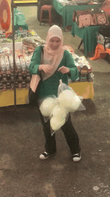 a woman in a hijab is holding a bag of cotton candy in front of a sign that says ' 0 '