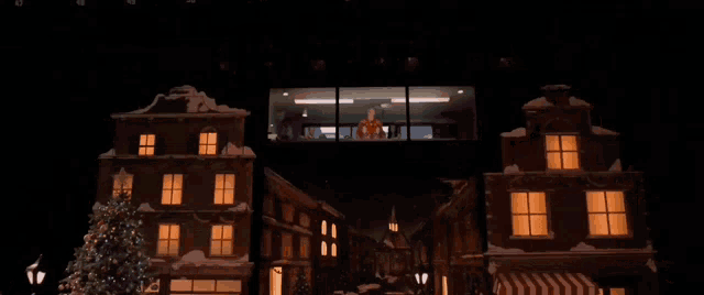 a man in a red sweater stands in front of a window overlooking a city at night