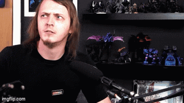 a man with long hair and a beard is sitting in front of a microphone in front of a shelf full of toys .