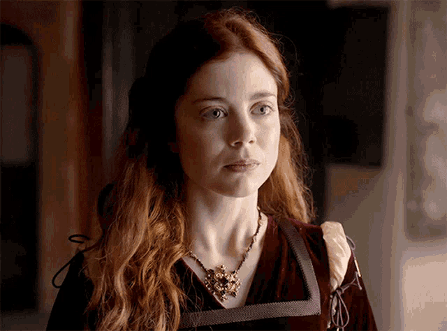 a woman with red hair is wearing a necklace and a red dress