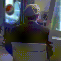 a man in a suit is sitting in a chair in front of a pepsi machine .