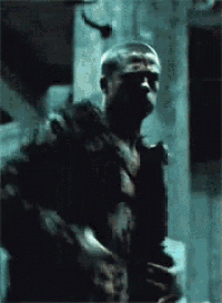 a man with a shaved head is standing in a dark room looking at something .