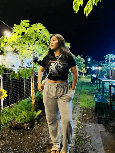 a woman wearing a black metallica t-shirt stands in a garden