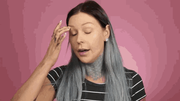 a woman with gray hair and a tattoo on her neck is touching her face .