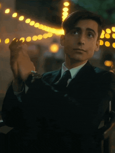 a young man in a suit and tie is sitting in a chair holding a cigarette .