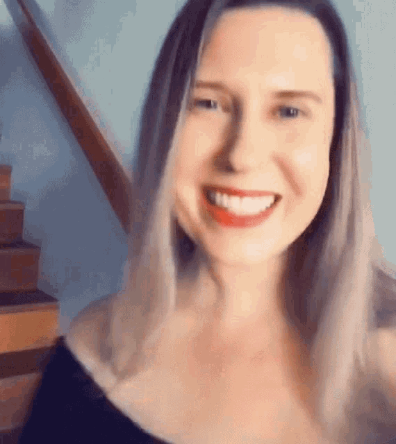 a woman in a black top is smiling in front of a set of stairs