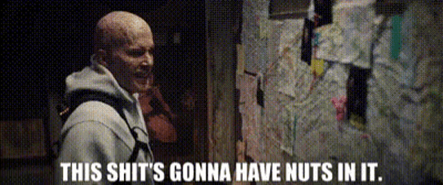 a bald man is standing in front of a wall that says this shit 's gonna have nuts in it .