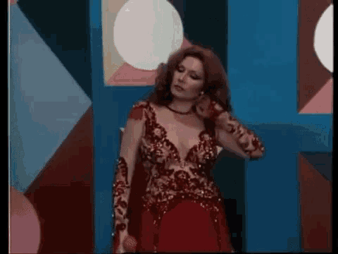a woman in a red dress and gloves is standing in front of a colorful wall .