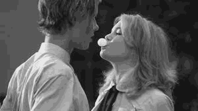 a man and a woman are blowing bubble gum and kissing .