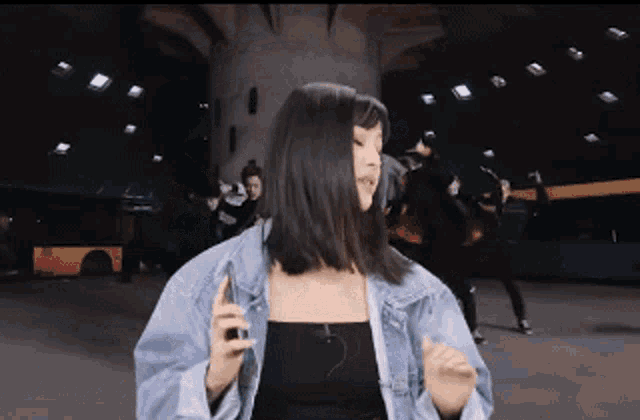 a woman wearing a denim jacket and a black tank top is dancing