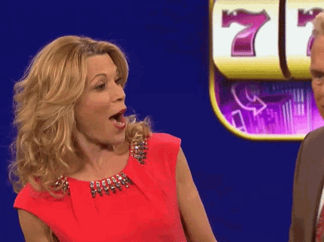 a woman in a red dress is standing in front of a slot machine that has the number 7 on it
