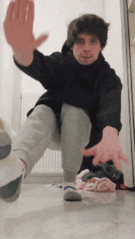 a man wearing a black hoodie and grey sweatpants is standing on one leg
