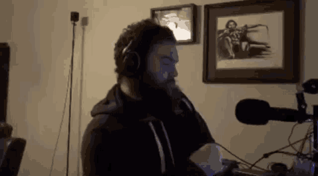 a man with a beard wearing headphones is standing in front of a microphone .