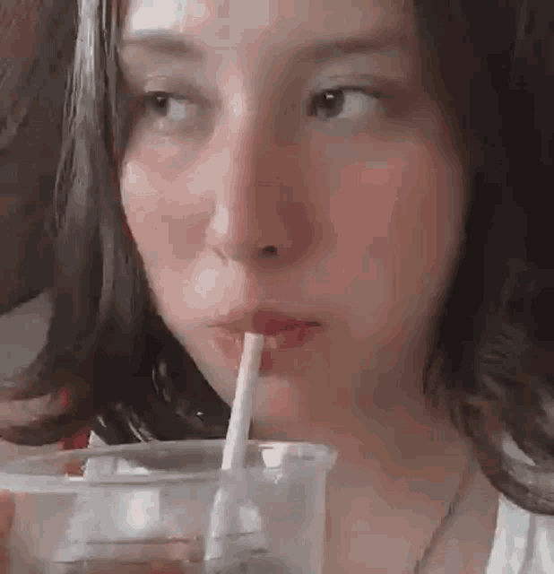 a woman is drinking a drink through a straw from a plastic cup .