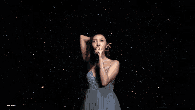 a woman in a white dress singing into a microphone with a watermark on the bottom right
