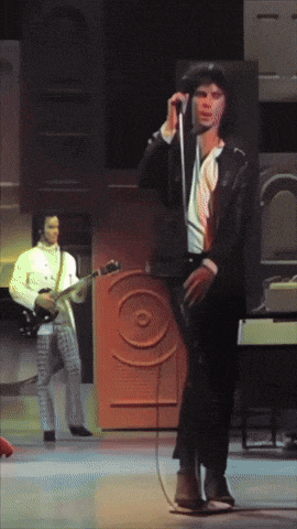 a man singing into a microphone while another man plays a guitar in the background