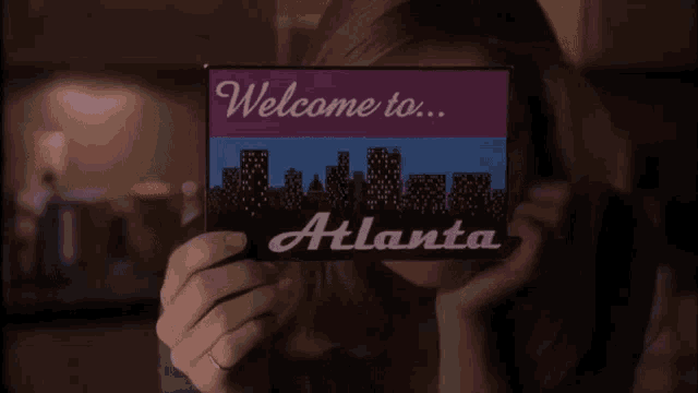 a woman is holding a welcome to atlanta sign in front of her face