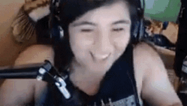 a woman wearing headphones and a black tank top is smiling while sitting in front of a microphone .