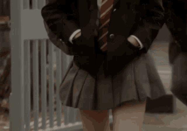 a woman in a school uniform is walking down the street and her skirt is blowing in the wind .