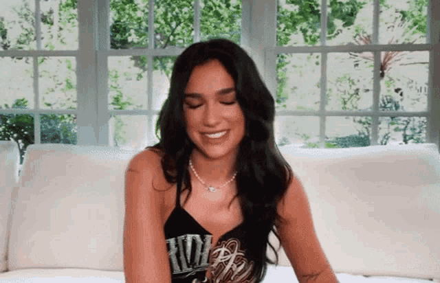 a woman is sitting on a couch wearing a black tank top that says rdw