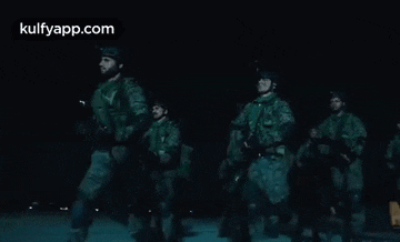 a group of soldiers are marching down a street at night .