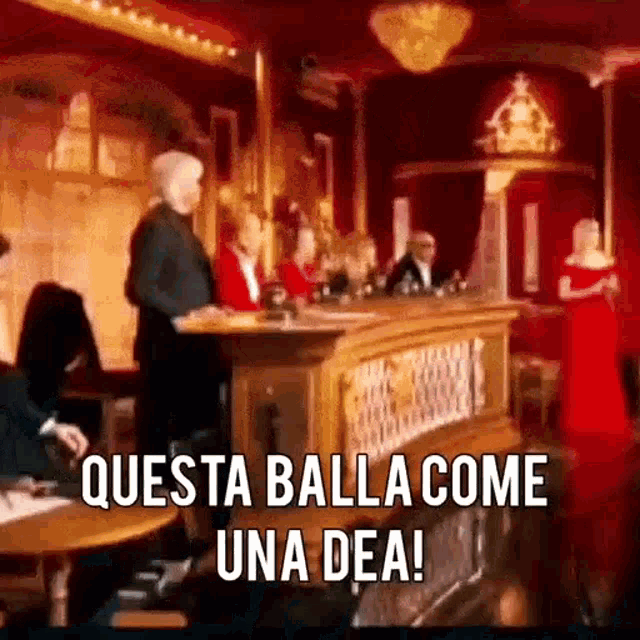 a group of people are sitting at a table in a room with a sign that says questa balla come una dea .