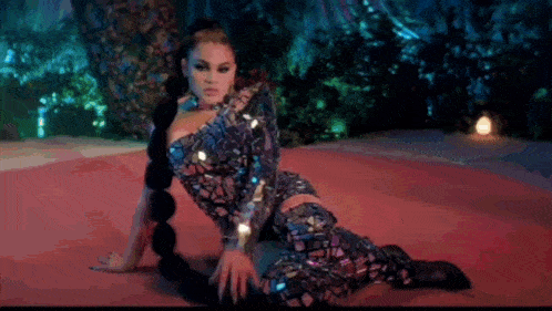 a woman in a sequined dress is kneeling on a red carpet