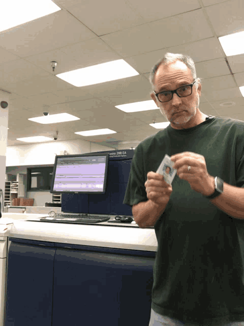 a man in a green shirt holds a card in front of a machine that says ' epson 280 ca ' on it